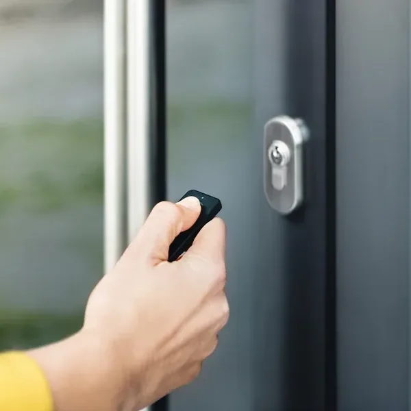 Mano che preme il telecomando Nuki Fob davanti a una porta d'ingresso