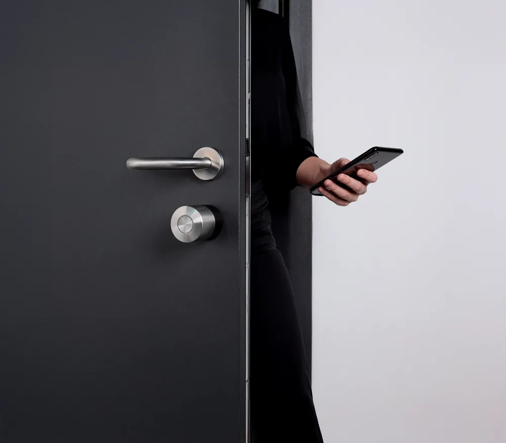 Porta scura con Smart Lock Pro e persona che la comanda dallo smartphone